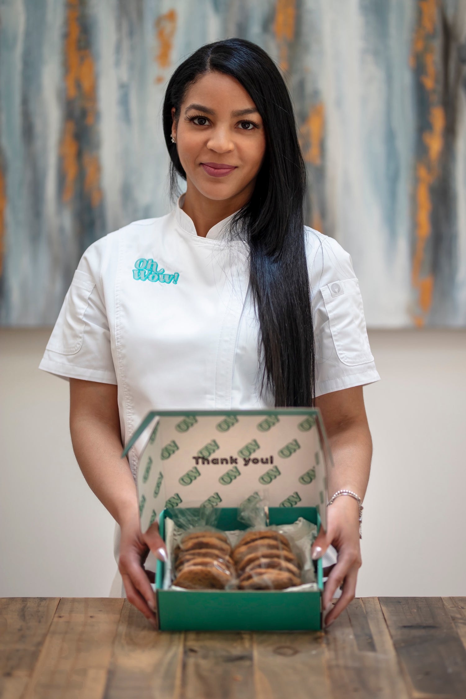 Woman with long hair in chef suit holding an open box of cookies